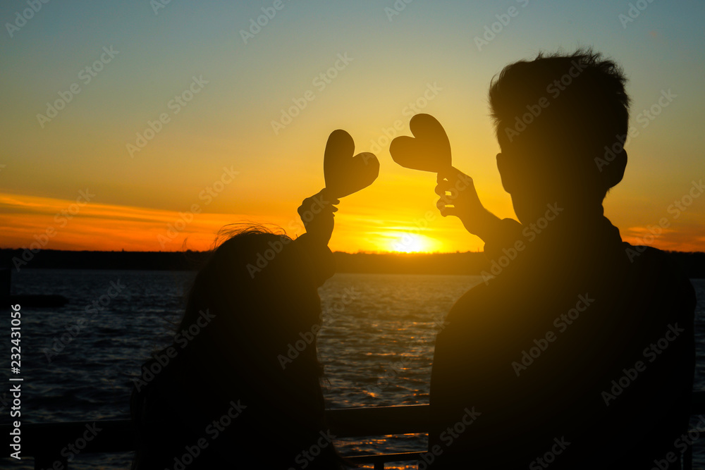 Happy young couple with decorative hearts on river bank at sunset