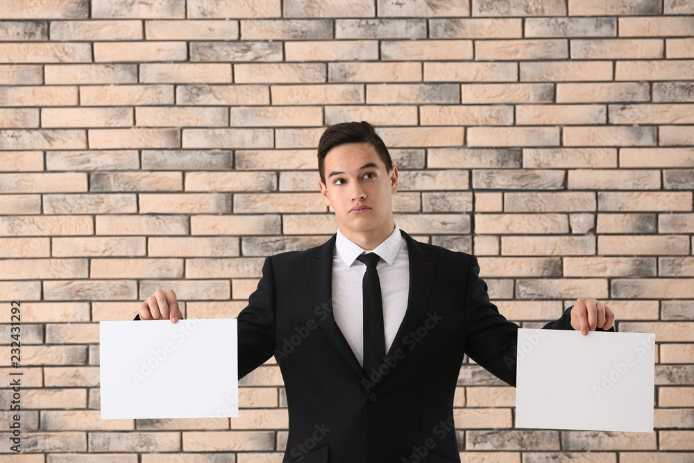 Handsome young businessman with blank sheets of paper against brick wall