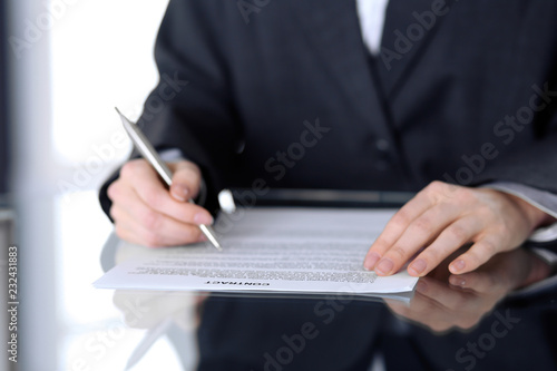 Close-up of female hands with pen over document, business concept. Lawyer or business woman at work in office
