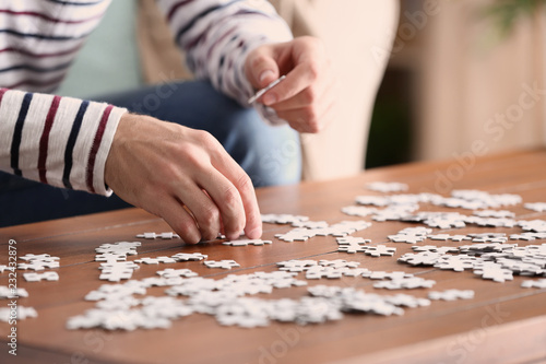 Young man doing jigsaw puzzle at home, closeup