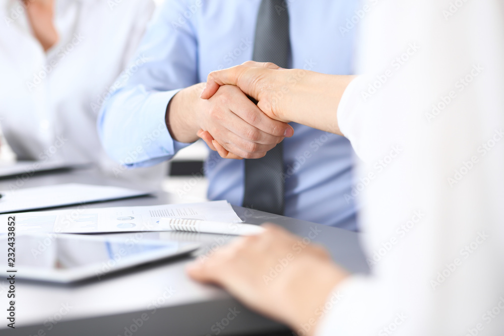 Obraz premium Close-up of business handshake at meeting or negotiation above the desk in office. Partners shaking hands while satisfied because signing contract or financial papers. Success concept