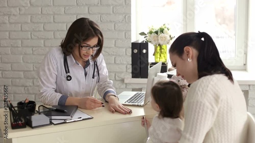 Beautiful young mother and her little daughter at the pediatrician. Portrait of a young pediatrician with glasses, she talks with her mother and a little girl in a children's hospital. photo