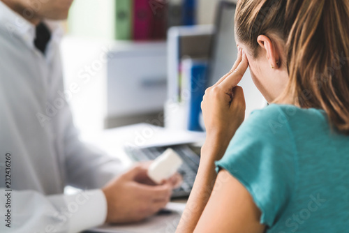 Doctor giving medical help to sick patient with bad headache or migraine. Physician or pharmacist holding bottle of pills and medicine in appointment. Woman suffering. Pain killers or antidepressants. photo