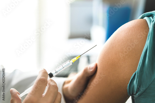 Doctor giving vaccine, flu or influenza shot  to patient with injection needle. Close up of arm and medical professional. Nurse or physician with syringe. Immunity, HPV or health care concept. photo