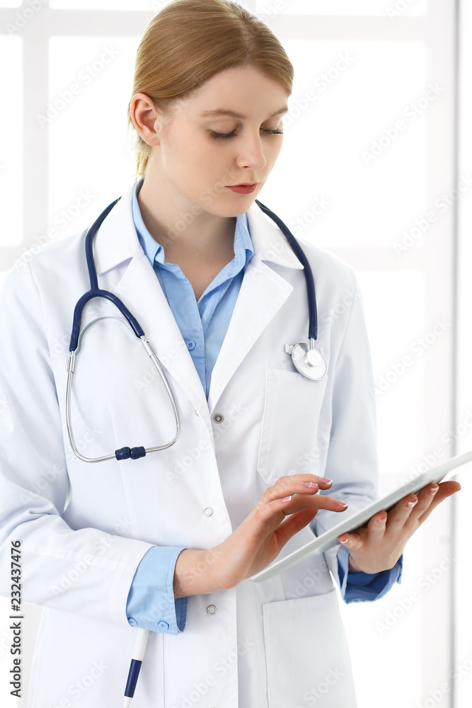 Doctor woman using tablet computer or touchpad with medical record form while standing near window in clinic or hospital. Medicine and healthcare concept. Physician at work Doctor woman using tablet computer or touchpad with medical record form while standing near window in clinic or hospital. Medicine and healthcare concept. Physician at work