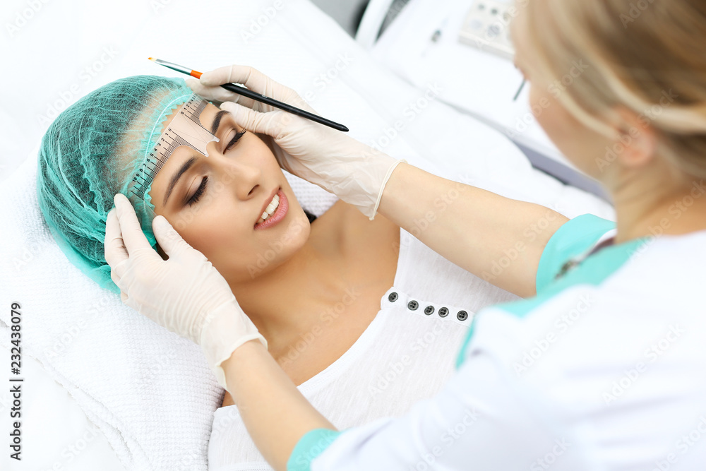 Professional beautician is going to correct eyebrow line at woman face using cosmetic ruler. Permanent brow makeup in beauty salon, closeup. Cosmetology treatment Professional beautician is going to correct eyebrow line at woman face using cosmetic ruler. Permanent brow makeup in beauty salon, closeup. Cosmetology treatment
