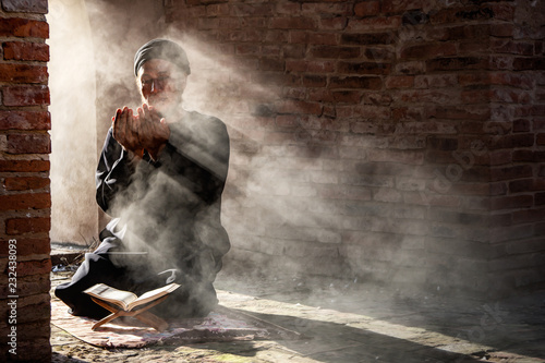 Fototapeta Silhouette of muslim male praying in old mosque with lighting and smoke backgrou