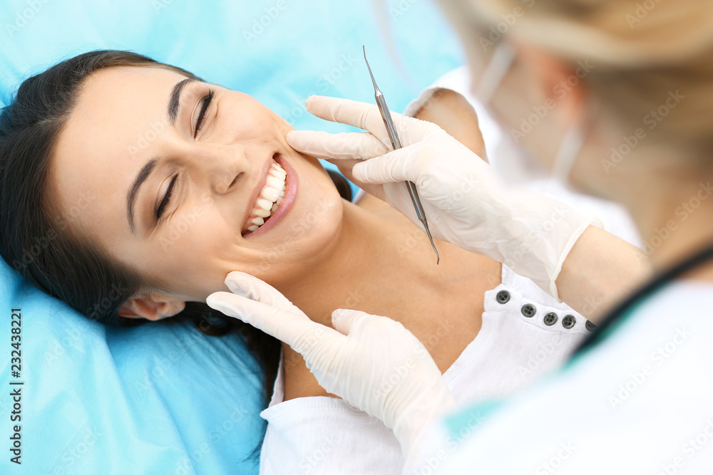 Young female patient visiting dentist office.Beautiful woman with healthy straight white teeth sitting at dental chair with open mouth during oral checkup while doctor working at teeth Young female patient visiting dentist office.Beautiful woman with healthy straight white teeth sitting at dental chair with open mouth during oral checkup while doctor working at teeth