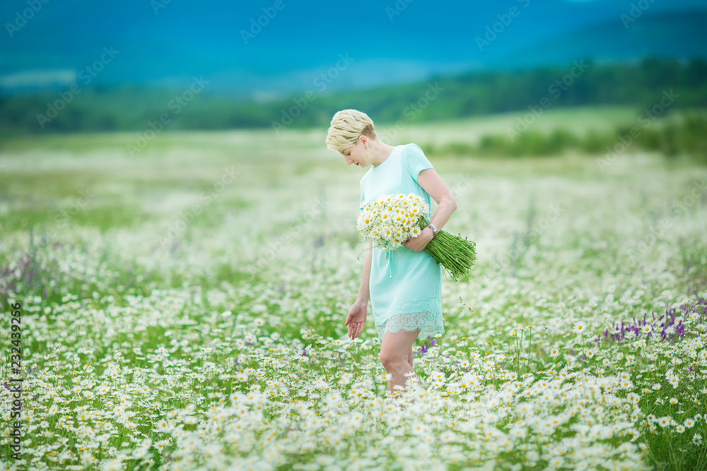 Attractive young woman with chamomile bouquet walking through the chamomile field. Active blonde outdoors