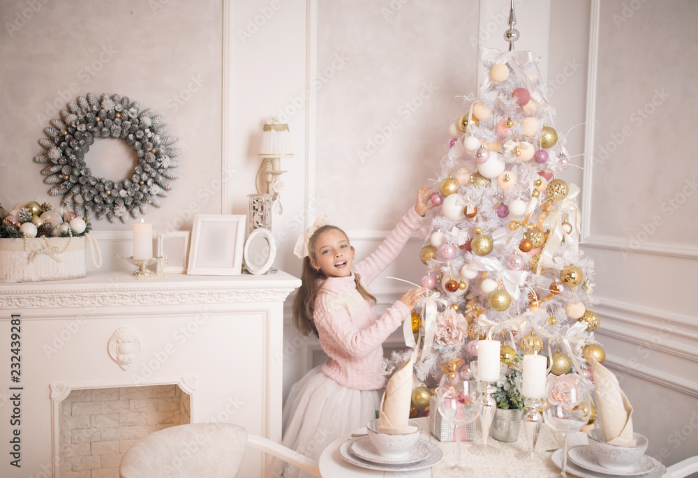 Beautiful little girl in a dress standing near the Christmas tree. Winter holidays. Happy New Year Beautiful little girl in a dress standing near the Christmas tree. Winter holidays. Happy New Year
