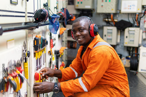 African marine engineer officer in engine control room ECR. He works in workshop and chooses correct tools and equipment photo