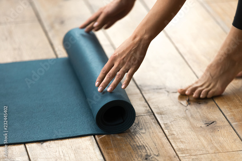 Fototapeta Naklejka Na Ścianę i Meble -  Fit beautiful woman folding blue exercise mat on wooden floor before or after working out in yoga studio club or at home Top close up view. Equipment for fitness, pilates or yoga, well being concept