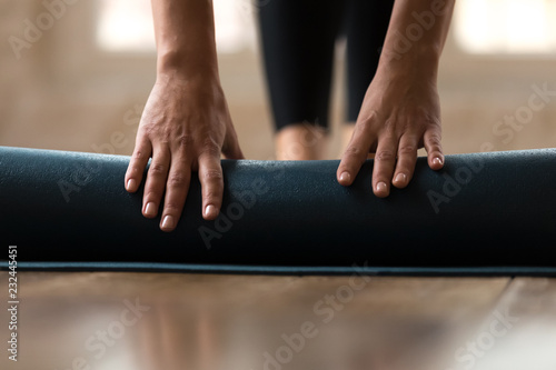 Front close up view of female hands rolling blue exercise mat on the floor before beginning her training session in yoga studio club at home. Equipment for fitness, pilates, yoga, well being concept