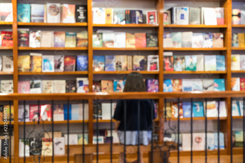 Blurred abstract background of bookshelves in book store, with a girl reading book in the store.