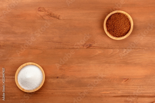 A photo of two bowls of white and brown sugar, shot from the top on a dark rustic wooden background with a place for text