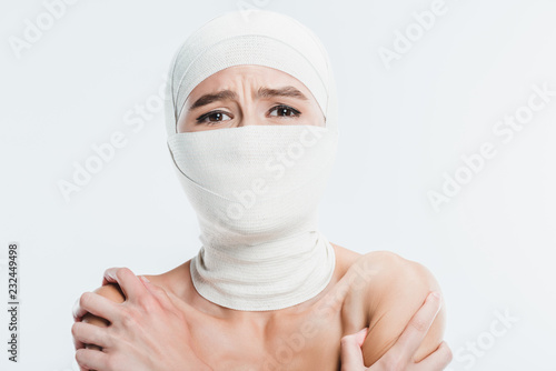 Fototapeta close up of naked painful woman with white bandages over face and head isolated