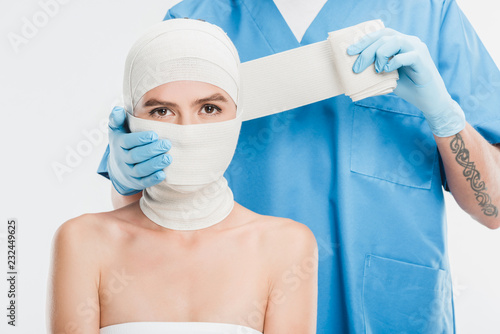 close up of plastic surgeon in gloves taping up woman face with bandage isolated on white