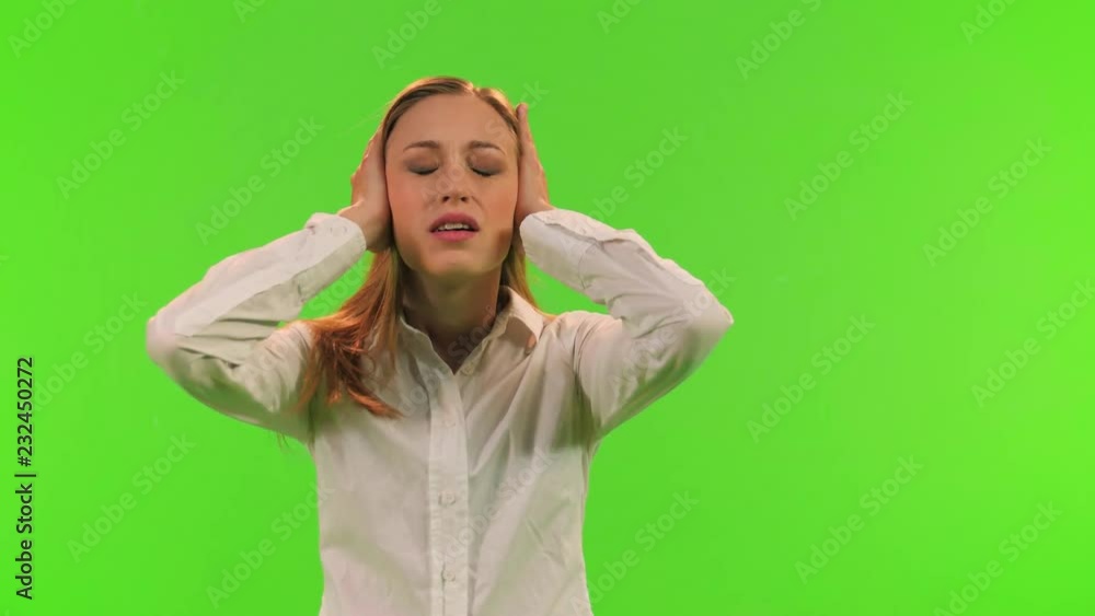 A disturb woman puts an earmuffs to protect her ears from noise, relaxes and smiles, over a green screen. A disturb woman puts an earmuffs to protect her ears from noise, relaxes and smiles, over a green screen.