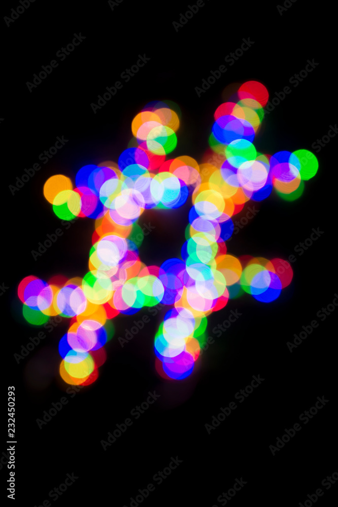 Holiday hashtag made from glowing defocus Christmas lights on a dark black night background