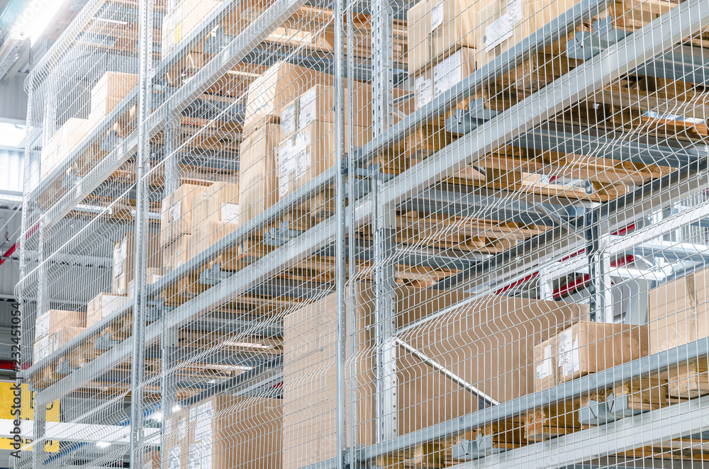 Large cardboard boxes on shelves closed metal mesh in a warehouse in an industrial enterprise. Warehouse technologies, employment at the factory. Arrangement of goods. Parcel delivery.