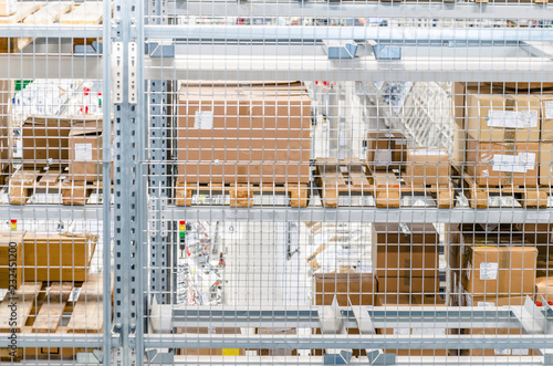 Large cardboard boxes on shelves closed metal mesh in a warehouse in an industrial enterprise. Warehouse technologies, employment at the factory. Arrangement of goods. Parcel delivery. © romankrykh