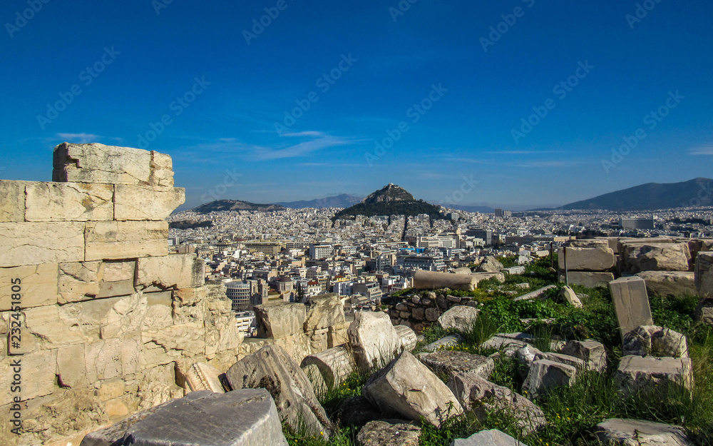 Athens from Acropolis showing ruins in a foreground and Mount Lycabettus surrounded by white buildings and blue sky