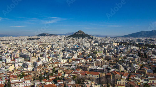 Athens from Acropolis showing Mount Lycabettus with white buildings architecture, mountain, trees, blue sky and floating white cloud background © nomadkate