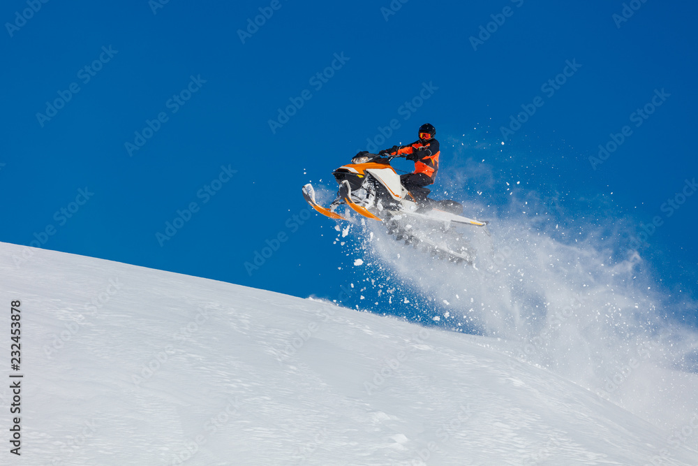 the guy is flying and jumping on a snowmobile on a background of blue sky leaving a trail of splashes of white snow. bright snowmobile and suit without brands. extra high quality 