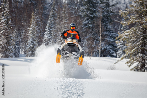 the guy is flying and jumping on a snowmobile on a background of winter forest  leaving a trail of splashes of white snow. bright snowmobile and suit without brands. extra high quality