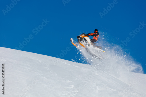 the guy is flying and jumping on a snowmobile on a background of blue sky leaving a trail of splashes of white snow. bright snowmobile and suit without brands. extra high quality 