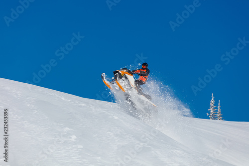 the guy is flying and jumping on a snowmobile on a background of blue sky leaving a trail of splashes of white snow. bright snowmobile and suit without brands. extra high quality 