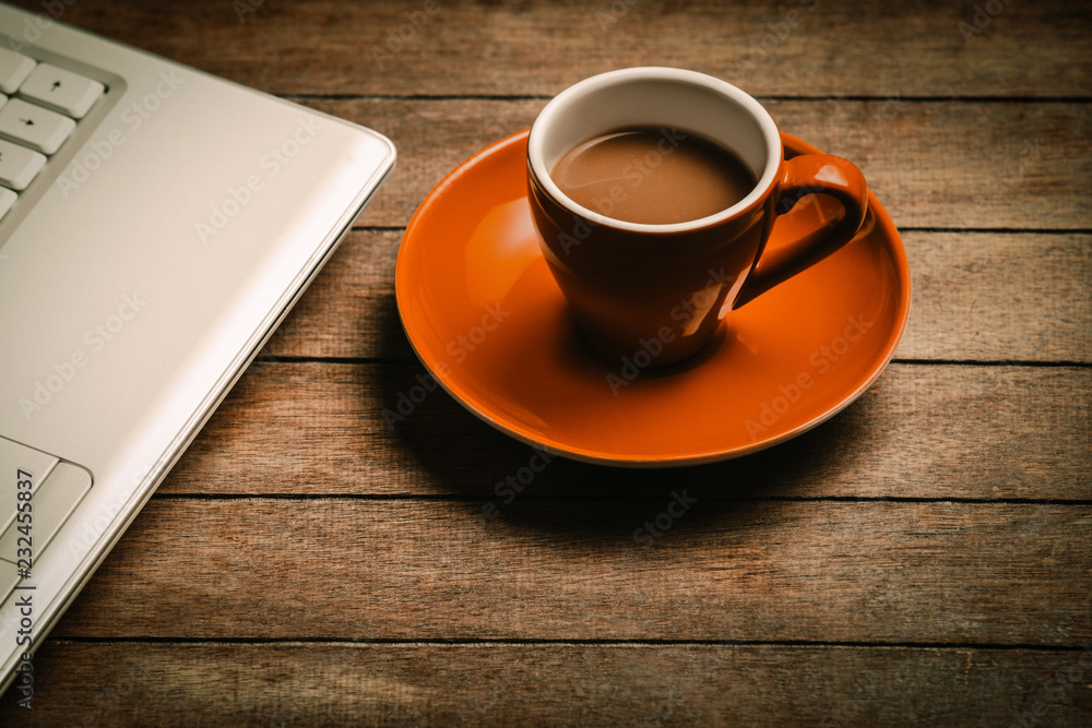 Obraz premium orange cup of coffee near laptop computer on wooden table. Side view