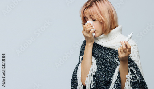 Studio portrait of cute unhealthy Caucasian woman with paper napkin sneezing, using nasal spray to help herself, experiences allergy symptoms, caught a cold. Rhinitis, cold, sickness, allergy concept photo