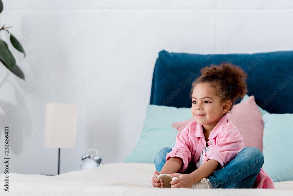 Smiling african american kid siting on the bed clasping her legs Smiling african american kid siting on the bed clasping her legs