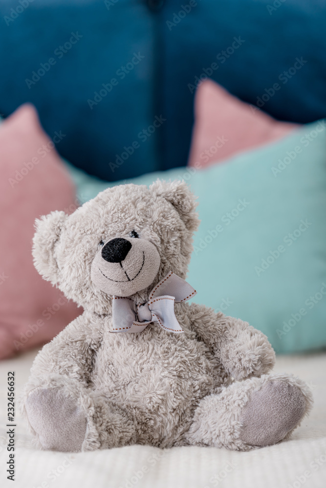 Close up vertical view of teddy bear sitting on the bed with pillows on background