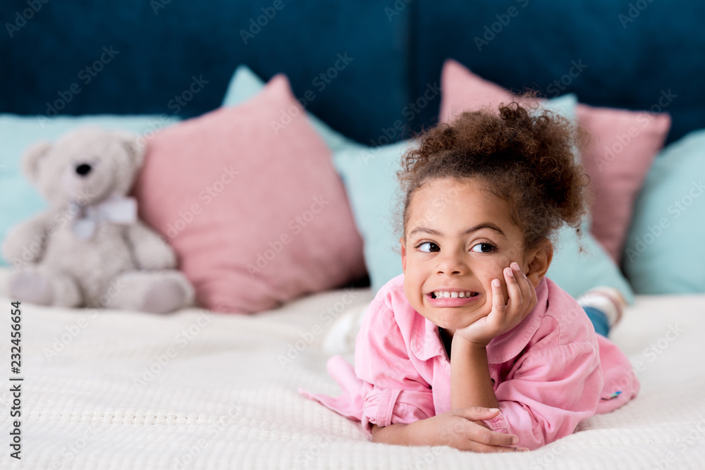 Adorable curly African american kid lying on the bed and smiling Adorable curly African american kid lying on the bed and smiling