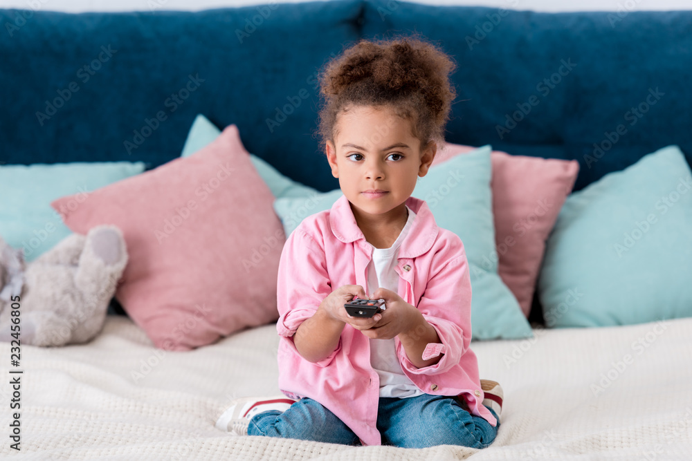 Cute African american child sitting on the bed and and switching channels Cute African american child sitting on the bed and and switching channels