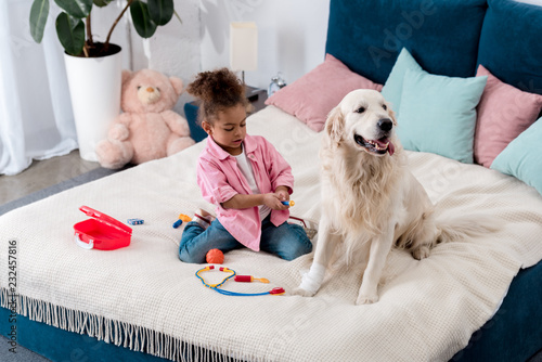 Curly african american kid playing doctor with her dog photo