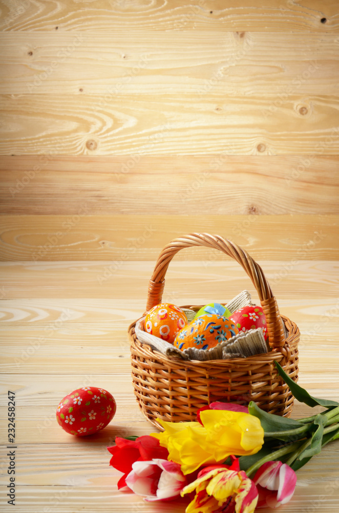 Easter eggs in wicker basket and colorful tulip flowers on wooden table background with space for text Easter eggs in wicker basket and colorful tulip flowers on wooden table background with space for text