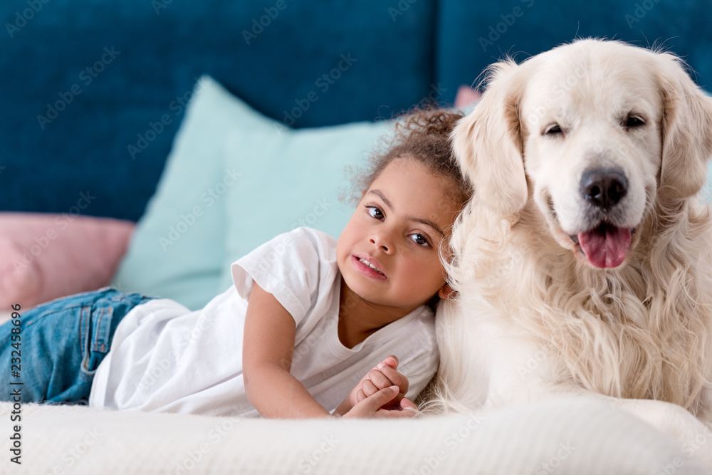 Adorable little african american kid with happy dog lying on bed Adorable little african american kid with happy dog lying on bed
