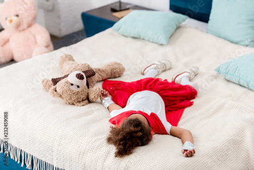 little child in red superhero costume with teddy bear lying on bed © LIGHTFIELD STUDIOS