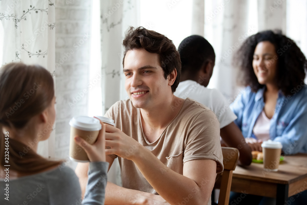 Diverse multi-ethnic couples sitting paired at table in cafe drinking hot beverages, coffee in paper cups, focus on caucasian smiling male. Friends spending time together or weekend activities concept Diverse multi-ethnic couples sitting paired at table in cafe drinking hot beverages, coffee in paper cups, focus on caucasian smiling male. Friends spending time together or weekend activities concept