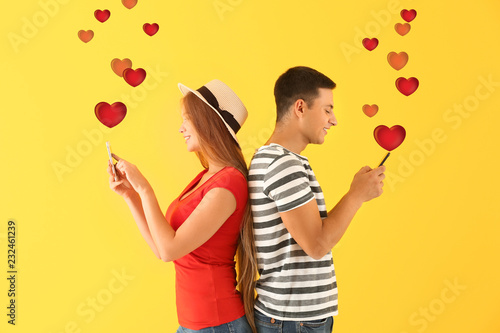 Young couple with mobile phones on yellow background. Online dating