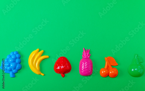 multicolored plastic toys fruits on a green background