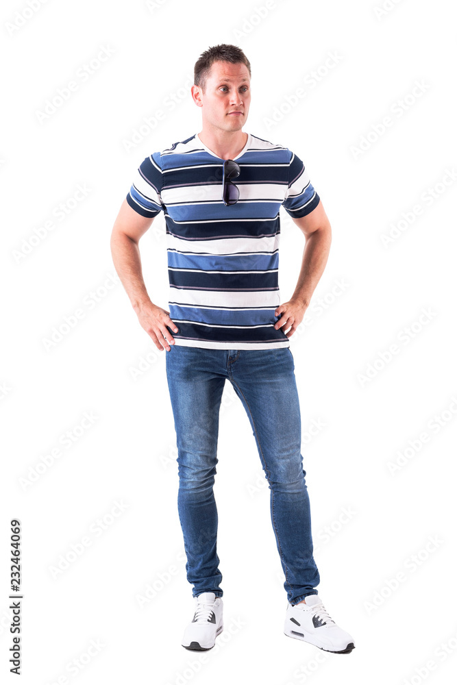 Confused young man in casual clothes with hands on hips looking away doubtfully. Full body isolated on white background. Confused young man in casual clothes with hands on hips looking away doubtfully. Full body isolated on white background.