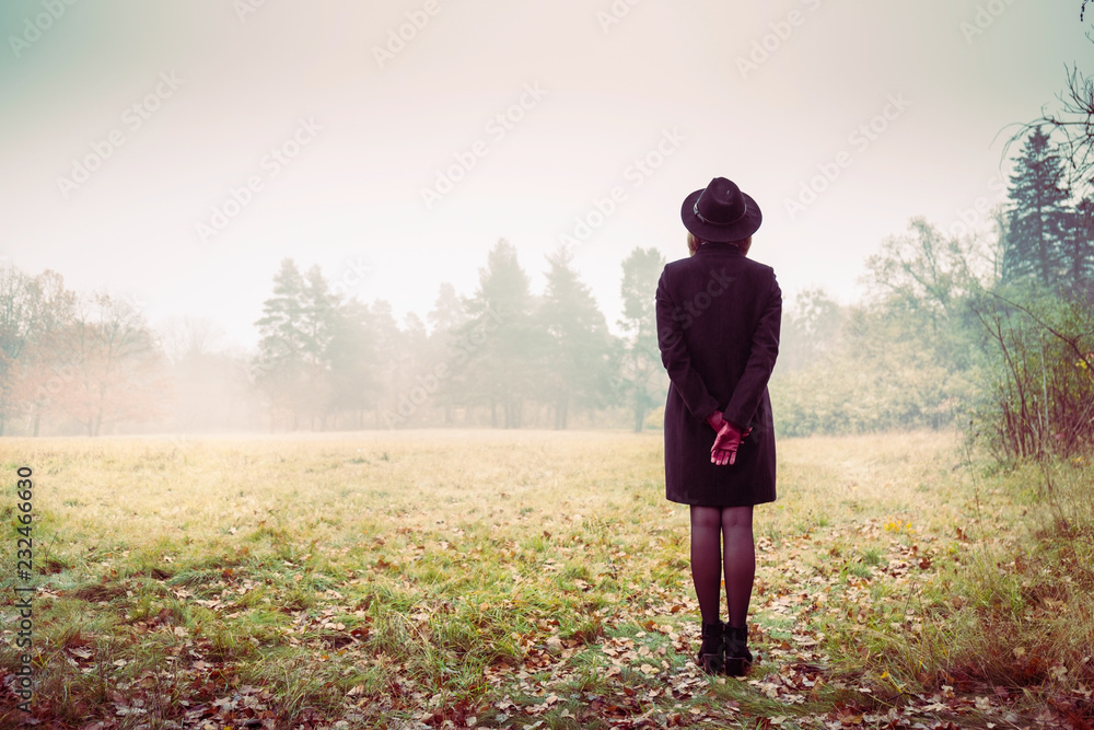 Girl in a coat and red gloves looks at the fog