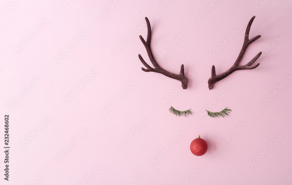 Fototapeta premium Christmas reindeer concept made of evergreen fir, red bauble decoration and antlers on pastel pink background. Minimal winter holidays idea. Flat lay top view composition.