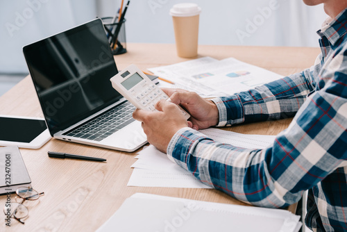 cropped shot of businessman with calculator working at workplace with documents and laptop