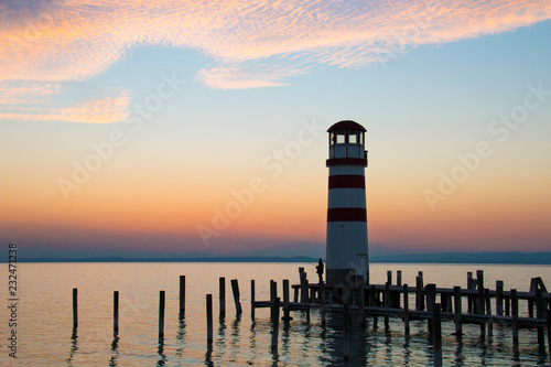 Low horizon romantic sunset sky over the lake landscape with red white lighthouse architecture and dock pillars in the water, beautiful warm colours of the largest lake in Central Europe, Neusiedl See