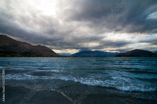 Dramatic landscape of tumultuous lake surrounded by mountains and stormy cloudy sky, gloomy weather, Central Otago, Queenstown Lake Wakatipu, New Zealand